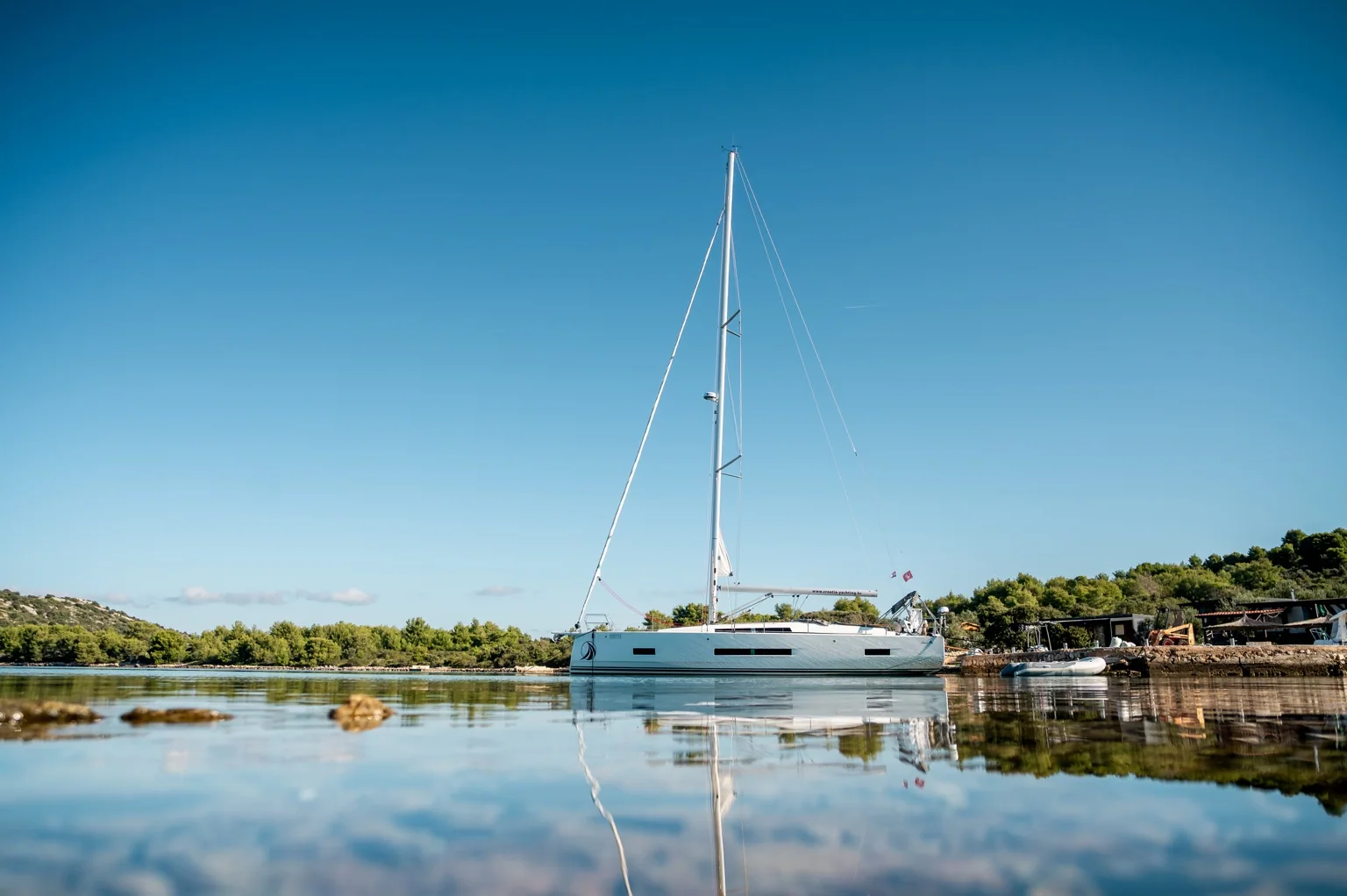 Infinity resting in a peaceful Adriatic bay, with the mast and its reflection visible